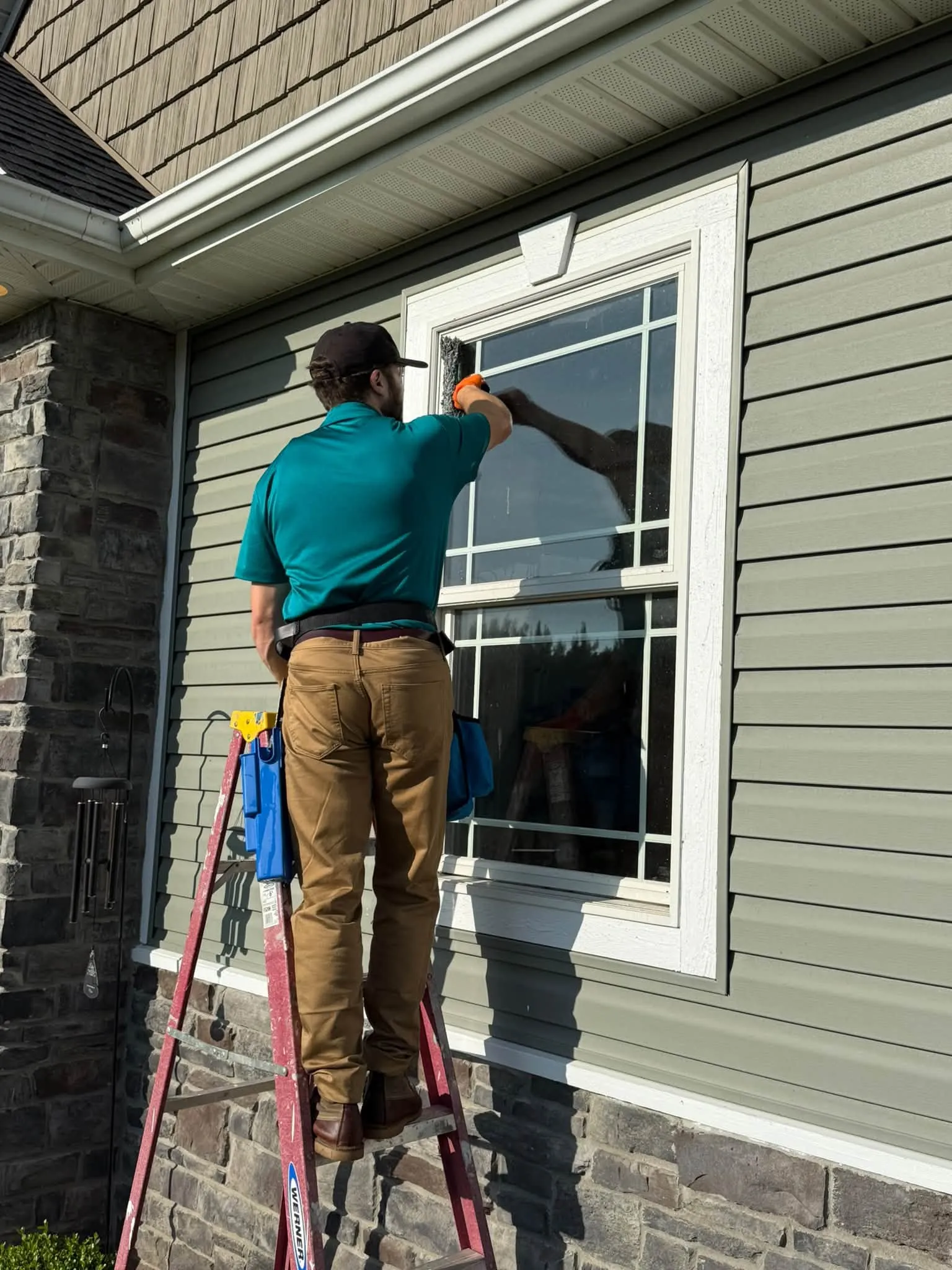 Fresh Start’s owner washing exterior window glass on a home with gray siding.